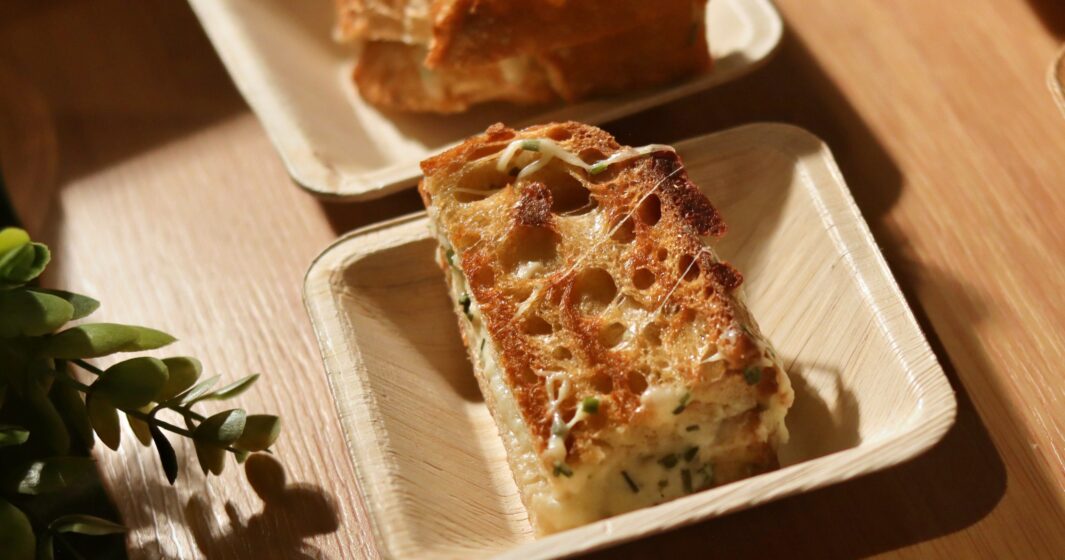 A grilled cheese sandwich slice with herbs on a small square plate, served on a wooden table.